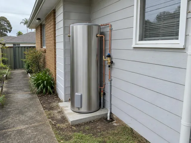 Outdoor stainless hot water system beside a house wall and window on a concrete pad in Riverwood